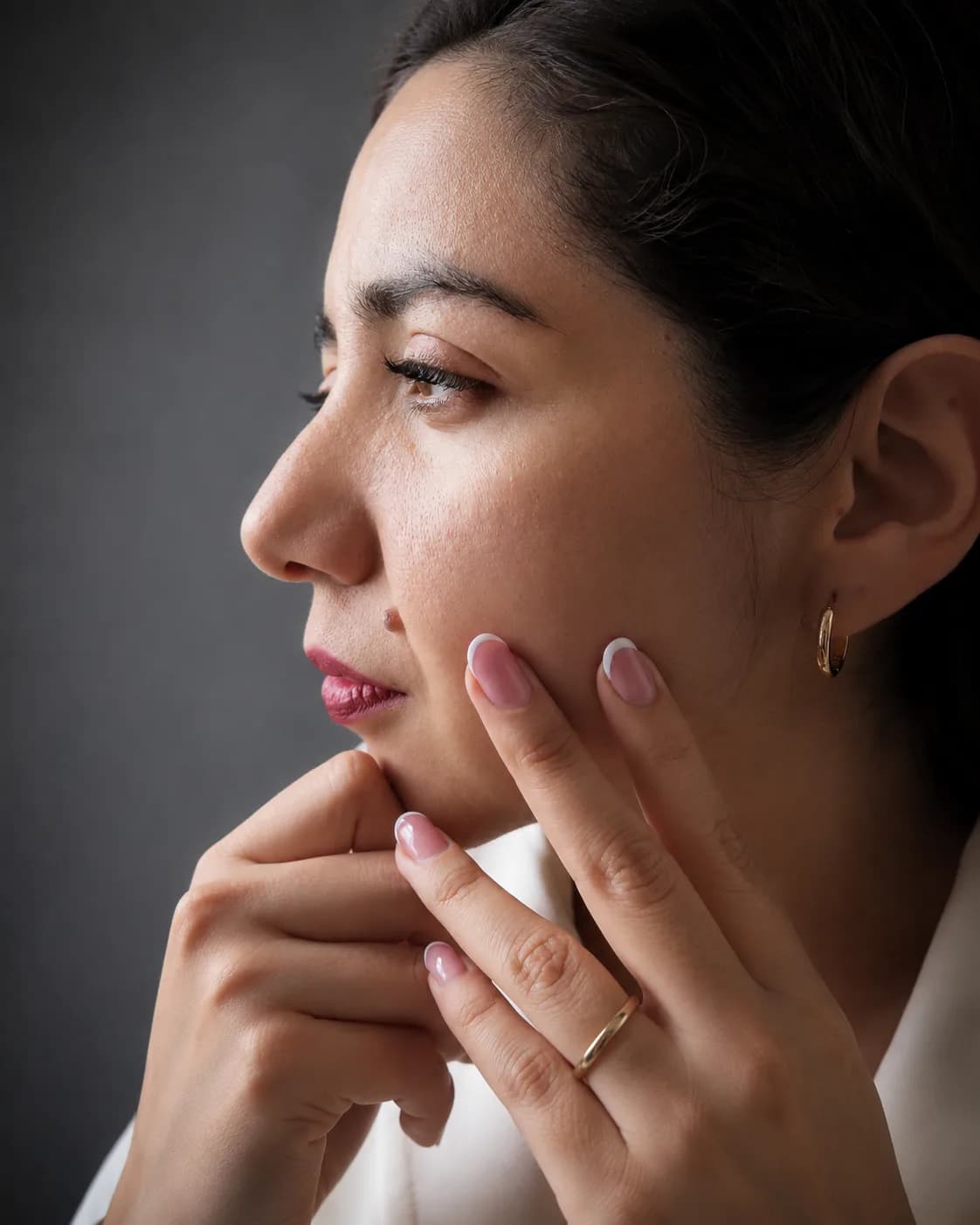 Retrato de perfil de una mujer con las manos apoyadas sobre el rostro, luz suave sobre fondo gris