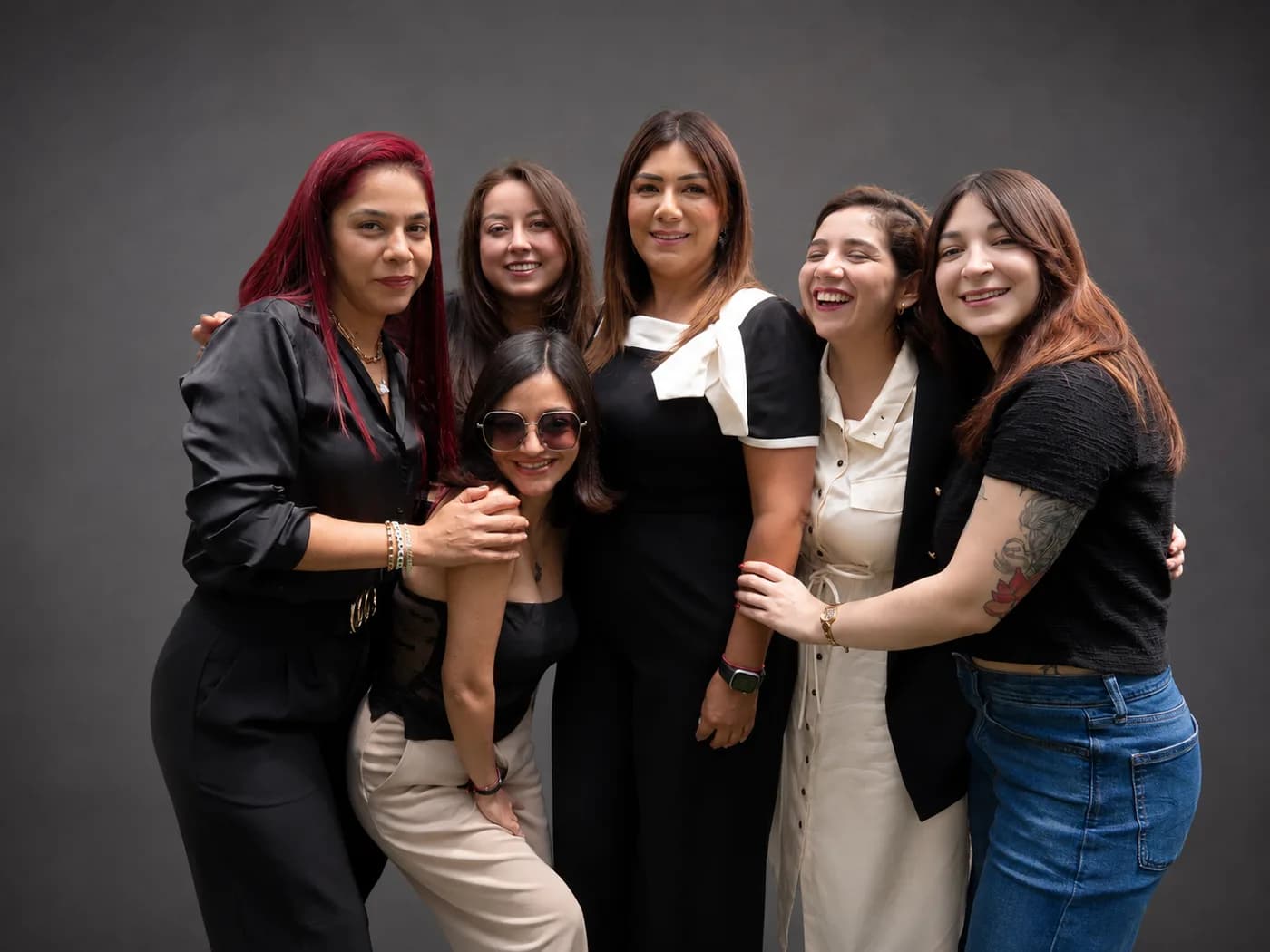 Seis mujeres de la comunidad Luma abrazadas en un retrato de estudio sobre fondo gris