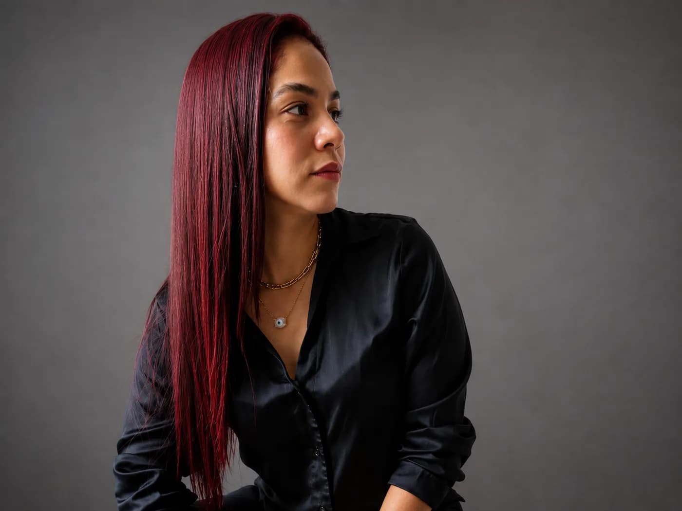 Mujer de cabello rojo largo y camisa negra de seda, mirando fuera de cuadro